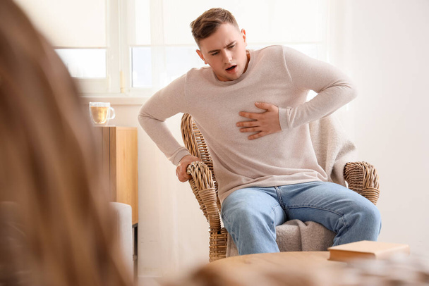 Young man suffering from chest pain in armchair at home - Photo, Image