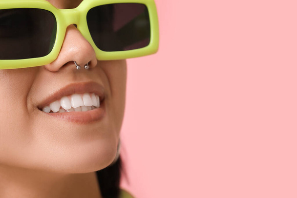 Stílusos fiatal nő napszemüvegben orrpiercing rózsaszín háttér, közelkép - Fotó, kép