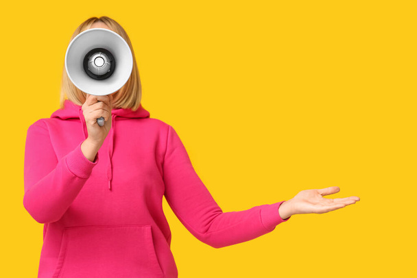 Dojrzała kobieta z megafonem wskazującym na coś na żółtym tle - Zdjęcie, obraz