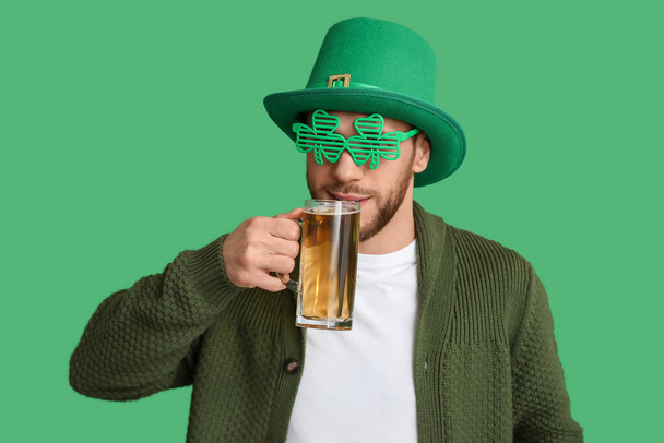 緑色の背景にビールのグラスとクローバーの形をしたレプチャン帽子と装飾的なメガネの若者. 聖パトリックの日のお祝い - 写真・画像