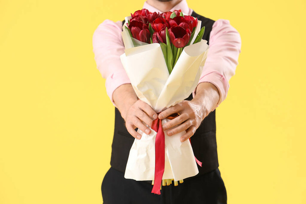 Funny young businessman with bouquet of tulips on yellow background, closeup. International Women's Day - Photo, Image