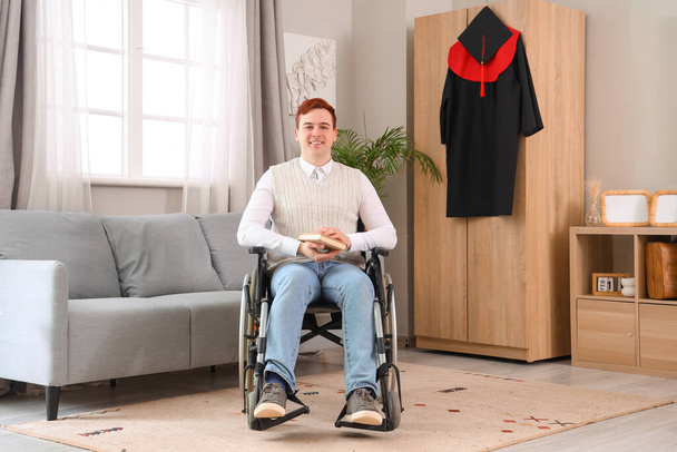 Mannelijke afgestudeerd in rolstoel met boek thuis - Foto, afbeelding