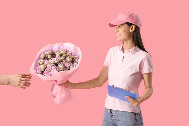 Young delivery woman giving bouquet of beautiful roses on pink background - Photo, Image
