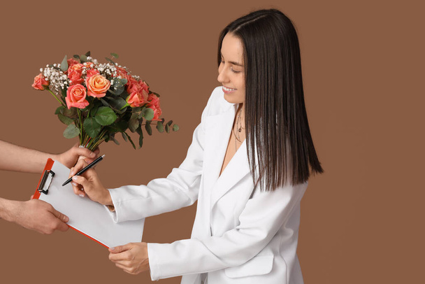 Jeune femme recevant bouquet de belles fleurs sur fond brun - Photo, image
