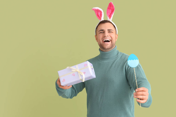 Joven feliz en orejas de conejo con caja de regalo y huevo de papel sobre fondo verde. Celebración Pascua - Foto, Imagen