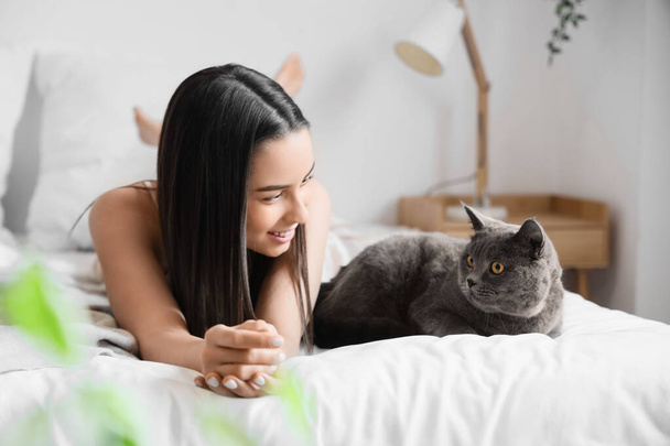 Jonge vrouw met schattig Brits Stenografisch kat liggend op bed thuis - Foto, afbeelding