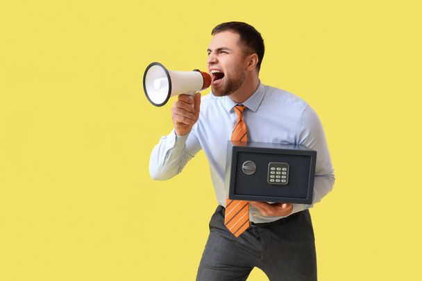 Молодой человек с сейфом и мегафоном кричит на желтом фоне - Фото, изображение