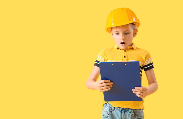 Шокированный маленький мальчик в каске с планшетом на желтом фоне - Фото, изображение