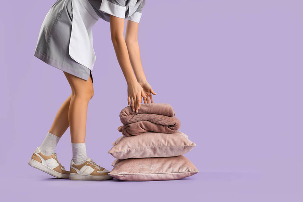 Vrouwelijke huishoudster met stapel kussens en warme ruitjes op lila achtergrond - Foto, afbeelding