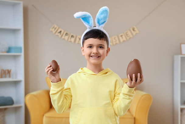 Lindo niño en orejas de conejito diadema con huevos de chocolate para Pascua en casa - Foto, Imagen