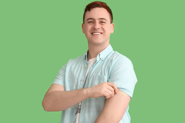 Young man with applied medical patch on green background. Vaccination concept - Photo, Image
