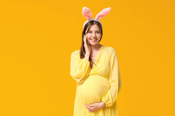 Mulher grávida bonita em orelhas de coelho no fundo amarelo. Celebração da Páscoa - Foto, Imagem