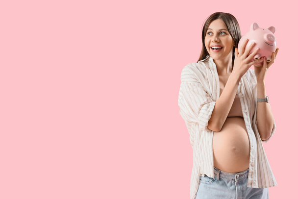 Junge schwangere Frau mit Sparschwein auf rosa Hintergrund. Konzept der Mütterrente - Foto, Bild