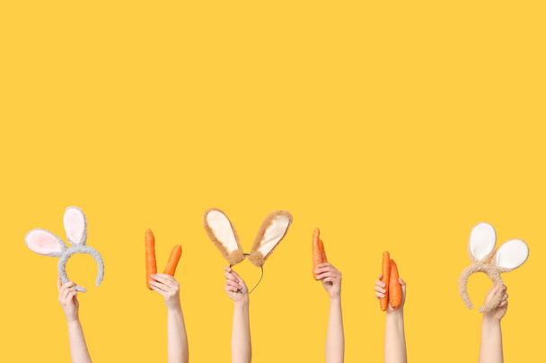 Kobiece dłonie trzymające uszy króliczka wielkanocnego opaski i marchewki na żółtym tle - Zdjęcie, obraz