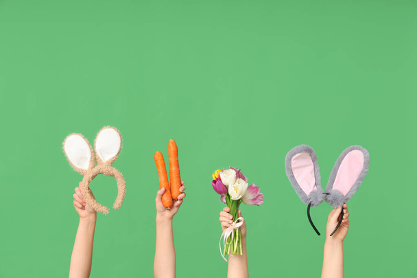 Mani femminili che tengono le fasce delle orecchie del coniglio di Pasqua con carote e tulipani su sfondo verde - Foto, immagini