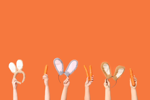 Kobiece ręce trzymające uszy króliczka wielkanocnego opaski i marchewki na pomarańczowym tle - Zdjęcie, obraz