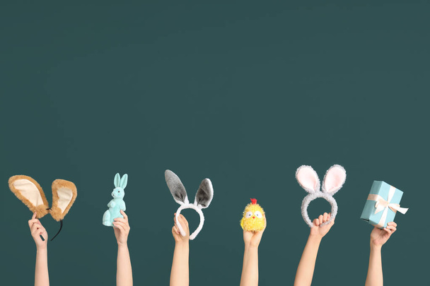 Vrouwelijke handen houden paashaas oren hoofdbanden met geschenkdoos, speelgoed kip en konijn op donkergroene achtergrond - Foto, afbeelding
