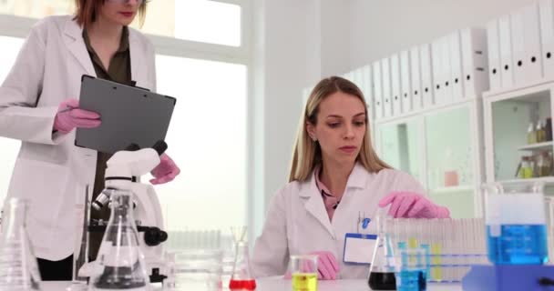 Lady assistente mostra i risultati dei test sugli appunti al collega scienziato in laboratorio chimico. Le donne controllano le registrazioni degli esperimenti nel centro medico - Filmati, video