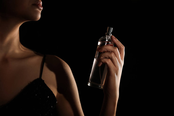 Pretty woman with bottle of perfume on black background - Photo, Image
