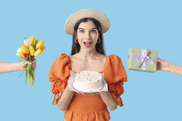 美しい若い女性は,青い背景にチューリップとギフトボックスの花束で甘い弁当ケーキと手を保持しています. 国際女性デー - 写真・画像