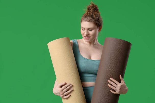 Спортивна молода жінка з йога килимками на зеленому фоні - Фото, зображення