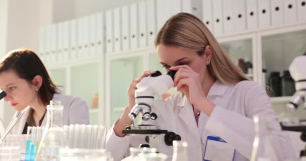 Las mujeres científicas estudian muestras de material con microscopios en el escritorio del laboratorio médico. Los técnicos utilizan dispositivos ópticos para estudiar la estructura celular - Metraje, vídeo