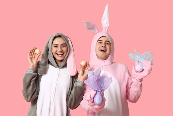 Hermosa pareja joven en traje de conejo con huevos de Pascua y regalos sobre fondo rosa - Foto, Imagen