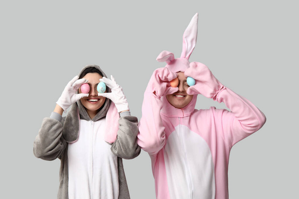 Красивая молодая пара в костюме кролика с пасхальными яйцами на сером фоне - Фото, изображение