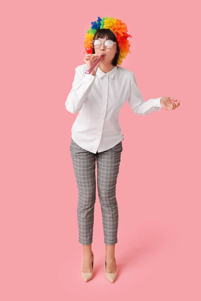 Funny young businesswoman with party blower on pink background. Fool's day - Foto, imagen