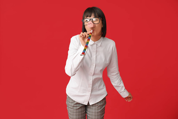 Funny young businesswoman with party blower on red background. Fool's day - Photo, Image