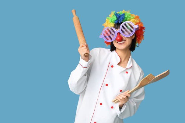 Funny young female chef with kitchen utensils on blue background. Fool's day - Photo, Image