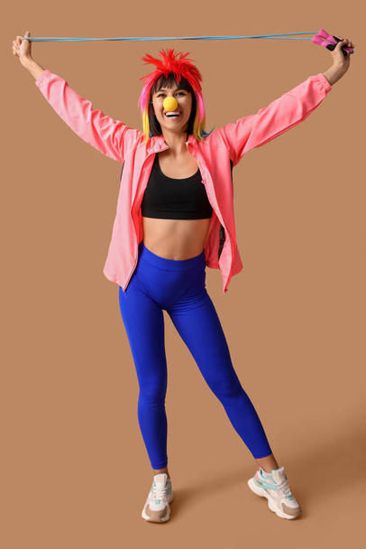 Young smiling female fitness trainer with jump rope on beige background. Fool's day - Photo, Image