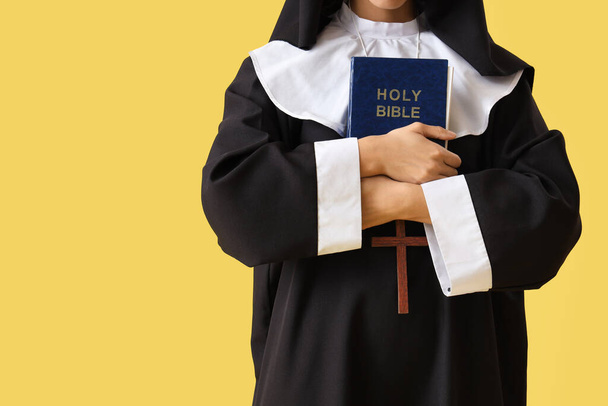 Joven monja con Biblia sobre fondo amarillo - Foto, imagen