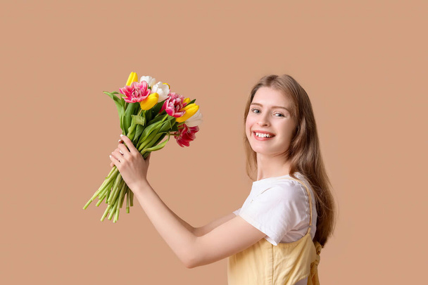 Щаслива молода жінка з букетом красивих тюльпанів на коричневому фоні - Фото, зображення