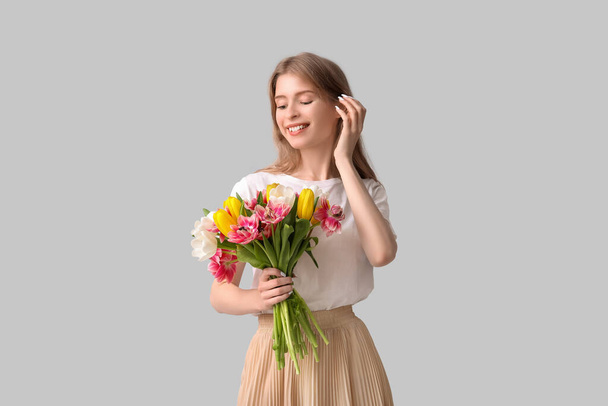 Happy young woman with bouquet of beautiful tulips on grey background - Photo, Image