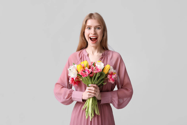 Surprised young woman with bouquet of beautiful tulips on grey background - Photo, Image