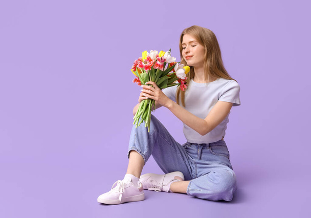 Bella giovane donna con bouquet di bei tulipani seduto sullo sfondo lilla - Foto, immagini