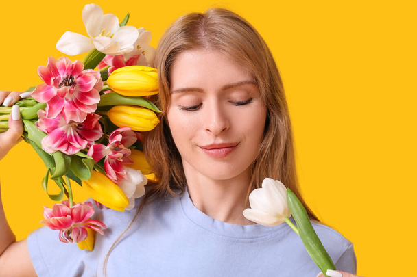 Pretty young woman with beautiful tulips on yellow background - Photo, Image
