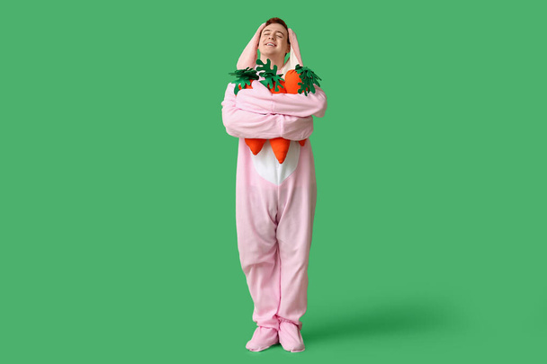 Feliz joven en traje de conejo de Pascua con zanahorias de felpa sobre fondo verde - Foto, Imagen