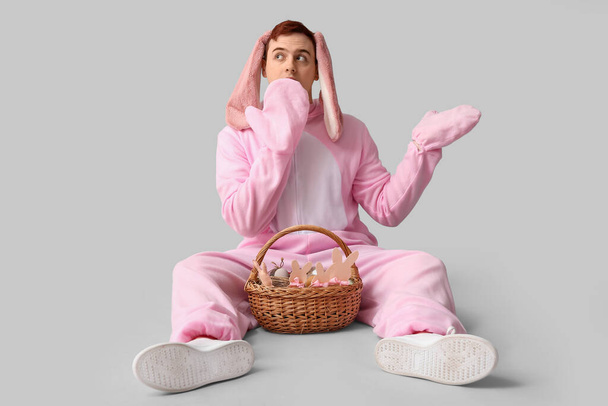 Surpris jeune homme en costume de lapin de Pâques assis avec panier sur fond blanc - Photo, image
