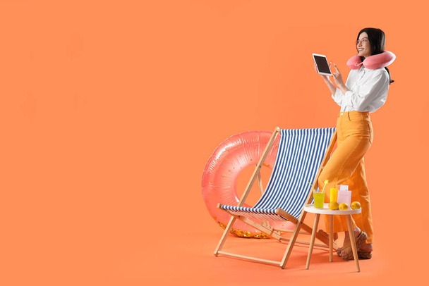 Young businesswoman with tablet computer and beach accessories ready for summer vacation on orange background - Photo, Image