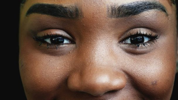 Een gelukkig jong zwart latina meisje met intense blik glimlachen op camera, macro close-up ogen van tiener vrouw - Foto, afbeelding