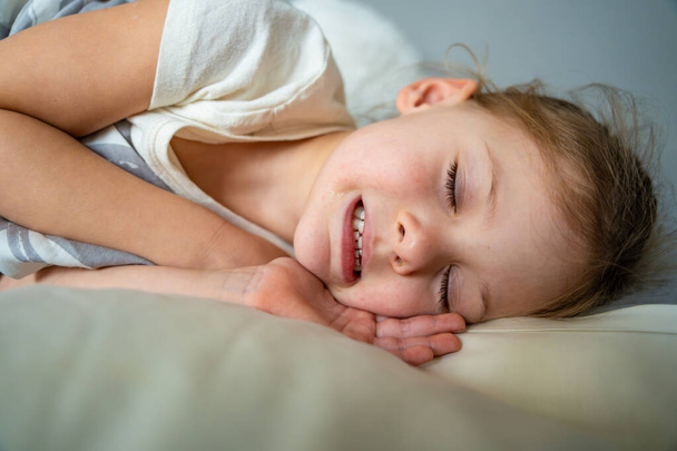 Χαριτωμένο κοριτσάκι κοιμάται και λείανση των δοντιών στα όνειρα, σφιγμένα δόντια με κούραση και άγχος. Υψηλής ποιότητας φωτογραφία - Φωτογραφία, εικόνα