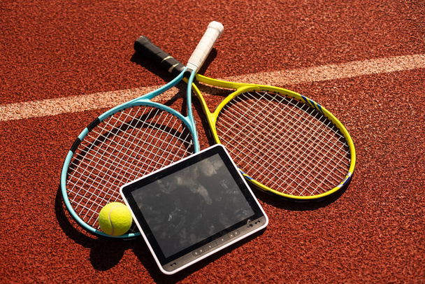 Tenis raketi ve topun yüksek açılı görüntüsü, kestane rengi arka planda dijital tablet. Yüksek kalite fotoğraf - Fotoğraf, Görsel