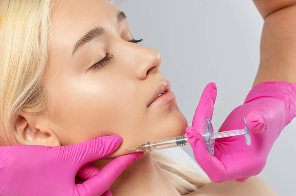 Cosmetoloog maakt verjongende anti rimpel injecties op het gezicht van een mooie vrouw. Vrouwelijke esthetische kosmetologie in een schoonheidssalon. - Foto, afbeelding