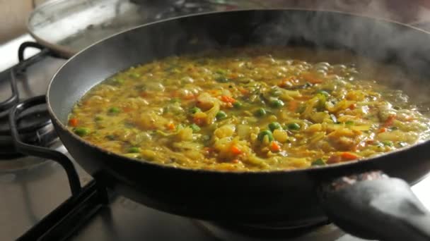 Una gran sartén de risotto burbujeante está hirviendo. Risotto con verduras y trozos de pollo se prepara en la cocina casera. - Metraje, vídeo