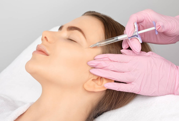 Cosmetologist makes rejuvenating anti wrinkle injections on the face of a beautiful woman. Female aesthetic cosmetology in a beauty salon. - Photo, Image