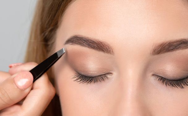 Maskenbildnerin zupft Augenbrauen in einem Schönheitssalon. Professionelle Make-up und Kosmetologie Hautpflege. - Foto, Bild