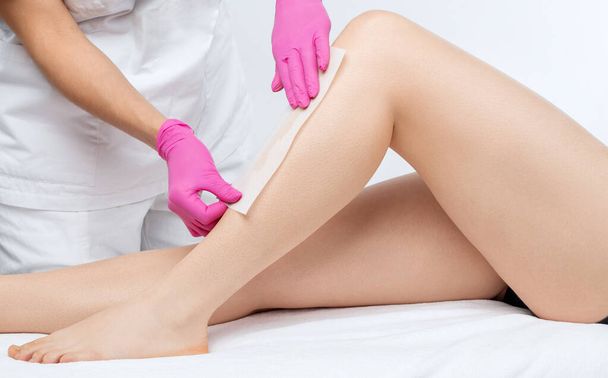 Eine Kosmetikerin macht in einem Schönheitssalon eine Epilation der Beine einer Frau mit Zuckerpaste. Weibliche ästhetische Kosmetologie. - Foto, Bild