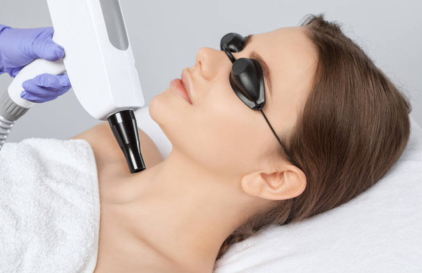 Beautician does laser carbon peeling on the problem areas of the skin of a young beautiful girl. Cosmetology and professional skin care. - Photo, Image